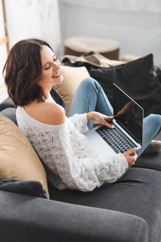 красива щаслива дівчина використовує ноутбук на дивані в затишній вітальні
 - Фото, зображення