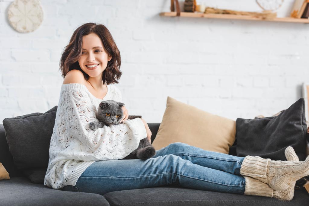 beautiful happy girl sitting on sofa with scottish fold cat   - Photo, Image