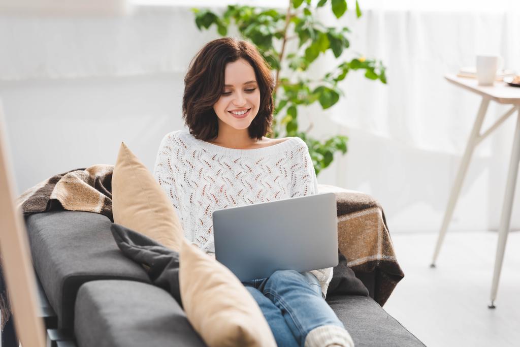 beautiful cheerful girl using laptop on sofa in cozy living room - Photo, Image