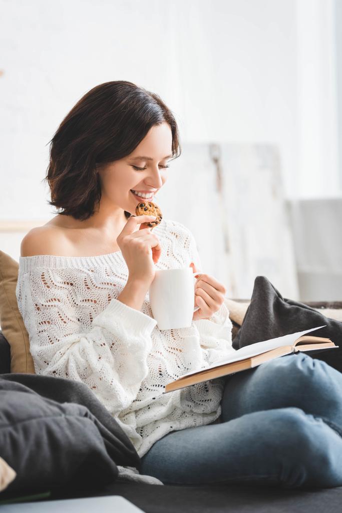 Kanepede kahve ve kurabiyelerle kitap okuyan mutlu kız. - Fotoğraf, Görsel