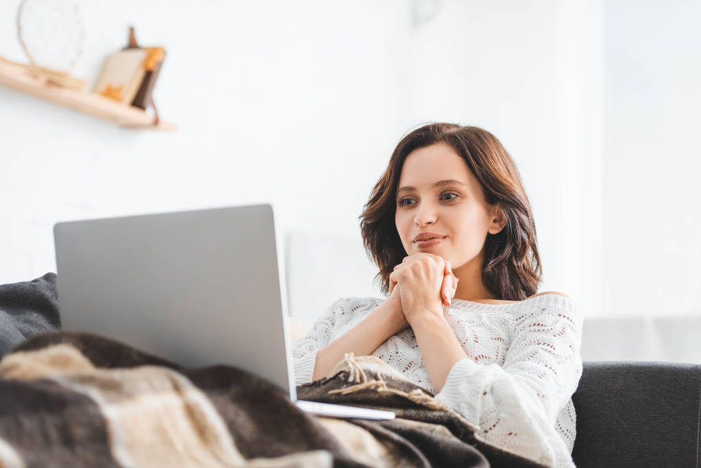 happy young woman in blanket using laptop on sofa in cozy living room - Photo, Image