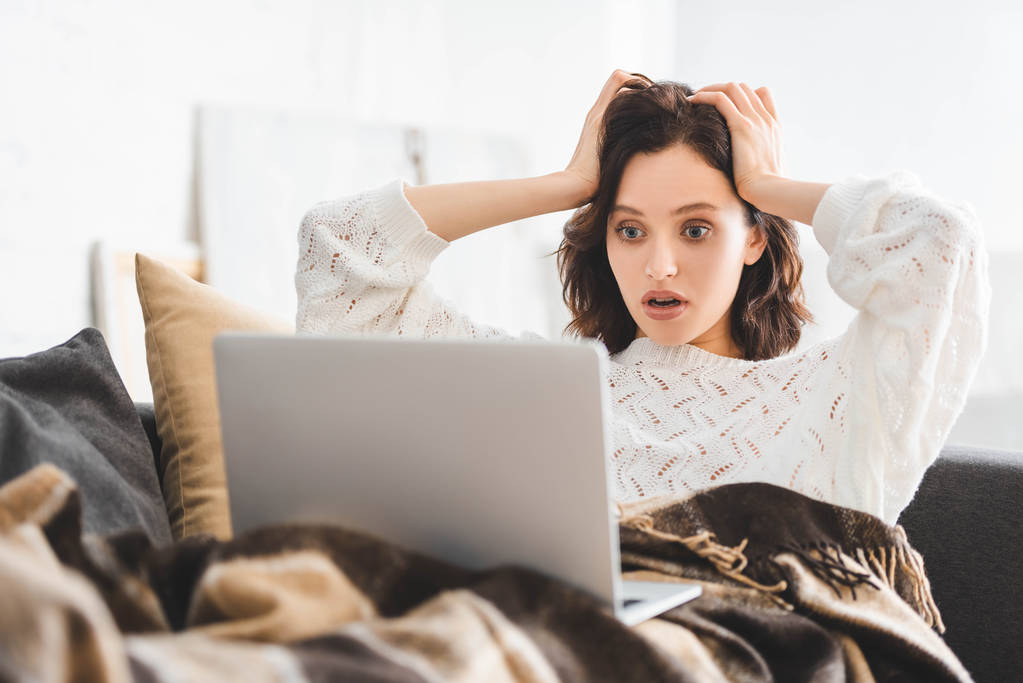 aggódó fiatal nő takaró használ laptop kanapén  - Fotó, kép