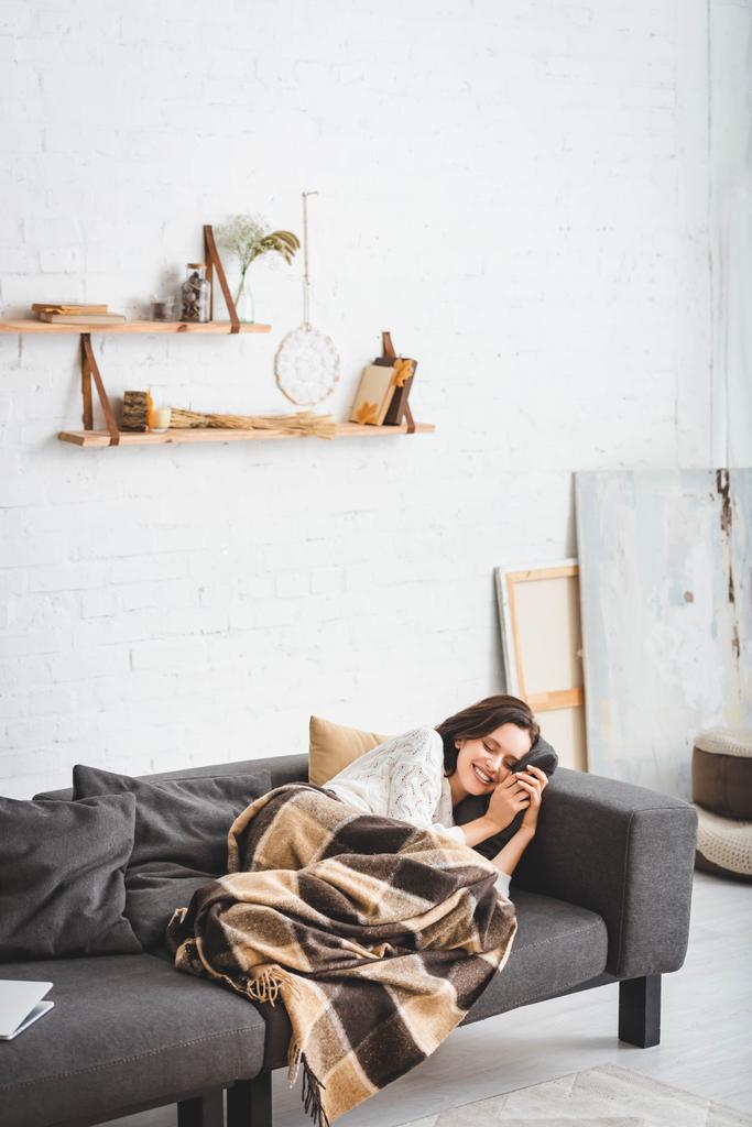 happy woman with closed eyes relaxing in blanket in cozy living room - Photo, Image