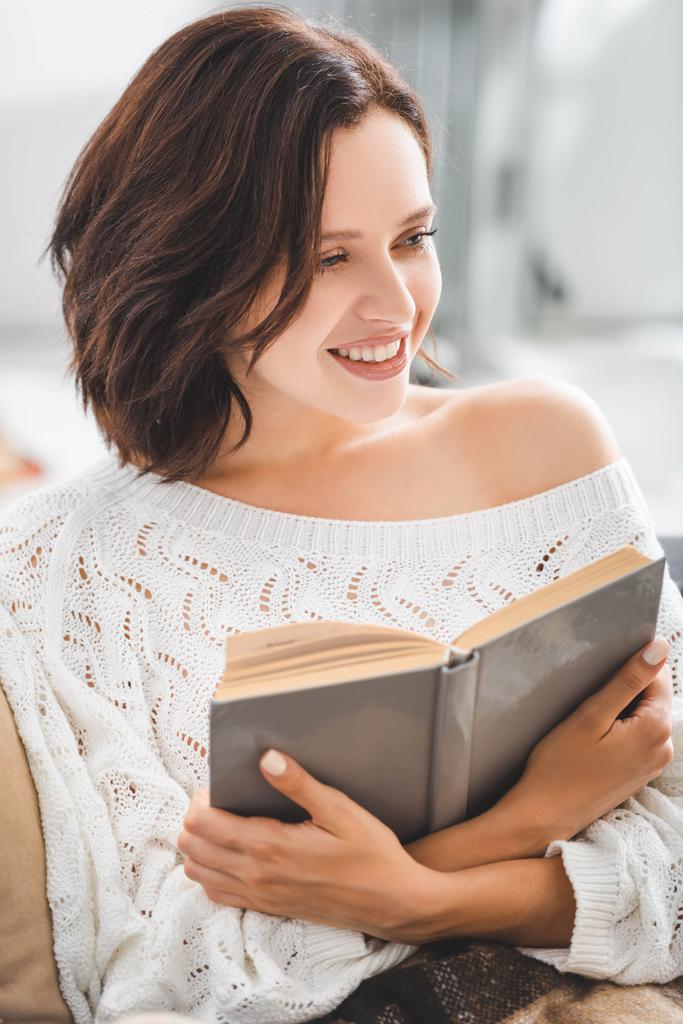 bela mulher sorridente leitura livro no sofá em casa
 - Foto, Imagem