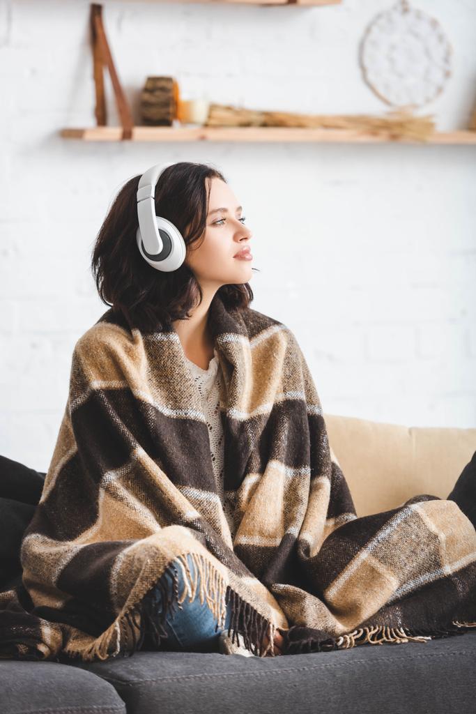 όμορφο κορίτσι που σκέφτεται και ακούει μουσική με ακουστικά, ενώ κάθεται σε κουβέρτα  - Φωτογραφία, εικόνα