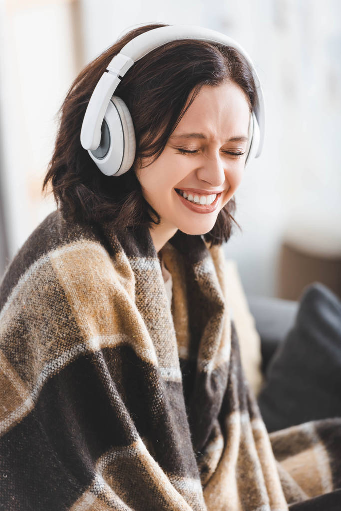 hermosa mujer sonriente con los ojos cerrados en manta escuchando música con auriculares
 - Foto, imagen