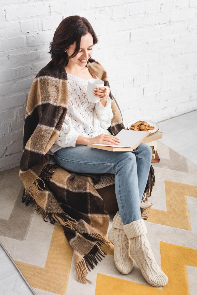 glückliches Mädchen in Decke Lesebuch in gemütlichem Wohnzimmer mit Kaffee und Keksen - Foto, Bild