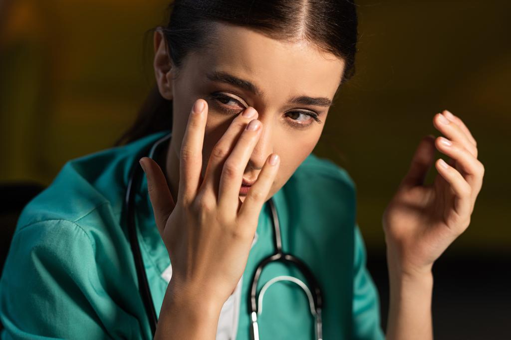 ελκυστική και κουρασμένη νοσοκόμα με στολή που κλαίει κατά τη διάρκεια της νυχτερινής βάρδιας - Φωτογραφία, εικόνα