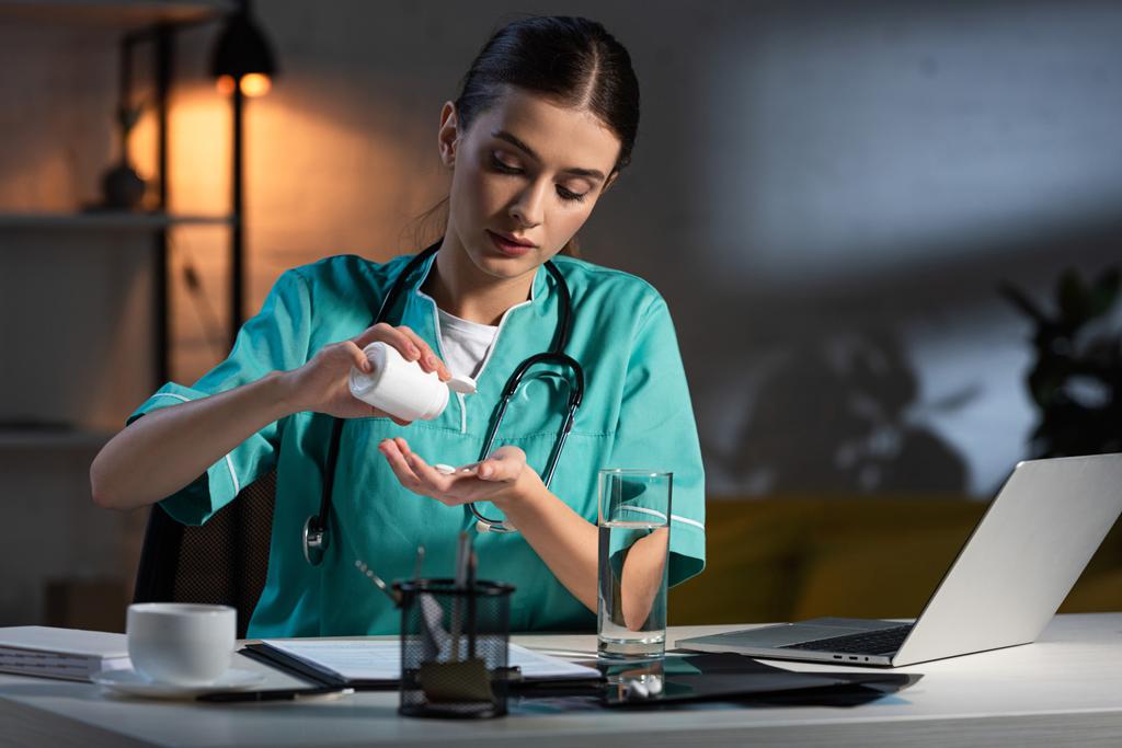 приваблива медсестра в уніформі сидить за столом і приймає таблетки під час нічної зміни
 - Фото, зображення