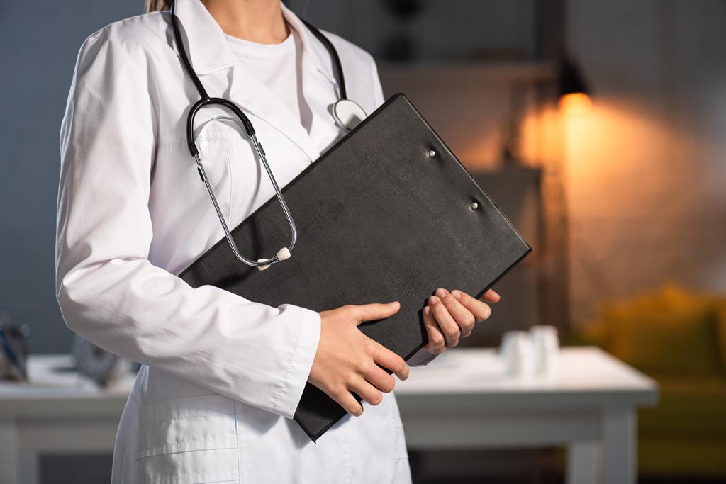 Ausgeschnittene Ansicht eines Arztes im weißen Kittel mit Klemmbrett während der Nachtschicht - Foto, Bild