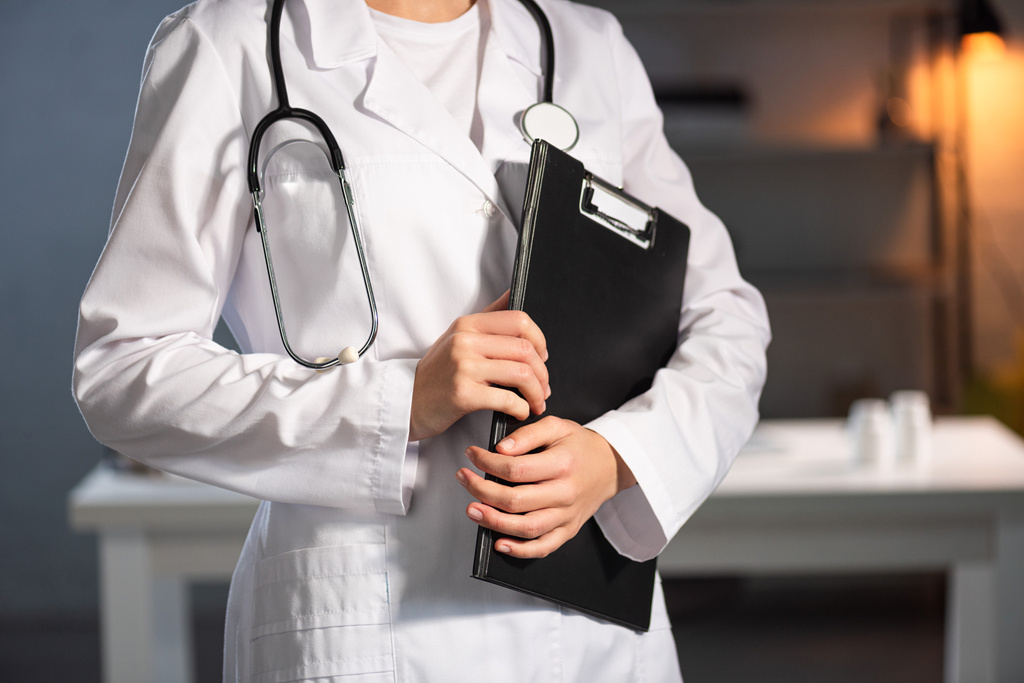 vista ritagliata del medico in camice bianco con stetoscopio che tiene appunti durante il turno di notte
 - Foto, immagini