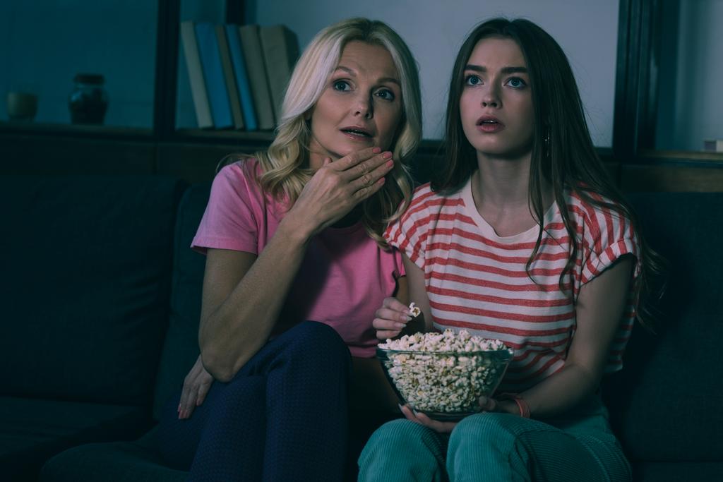 keskittynyt äiti ja tytär katsomassa televisiota ja syö popcornia
  - Valokuva, kuva