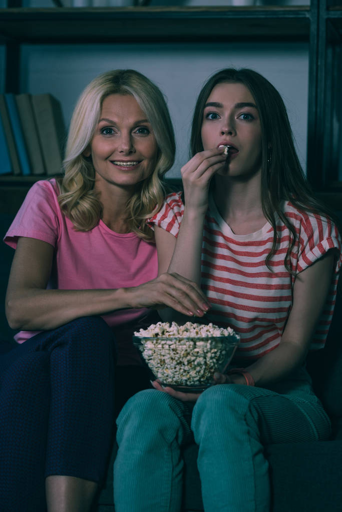 madre e figlia positive guardando la fotocamera mentre mangiano popcorn
 - Foto, immagini