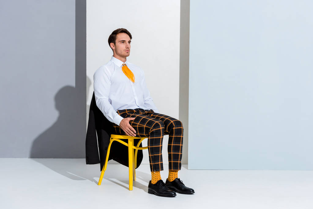 молодой человек сидит на желтом стуле на белом и сером
  - Фото, изображение