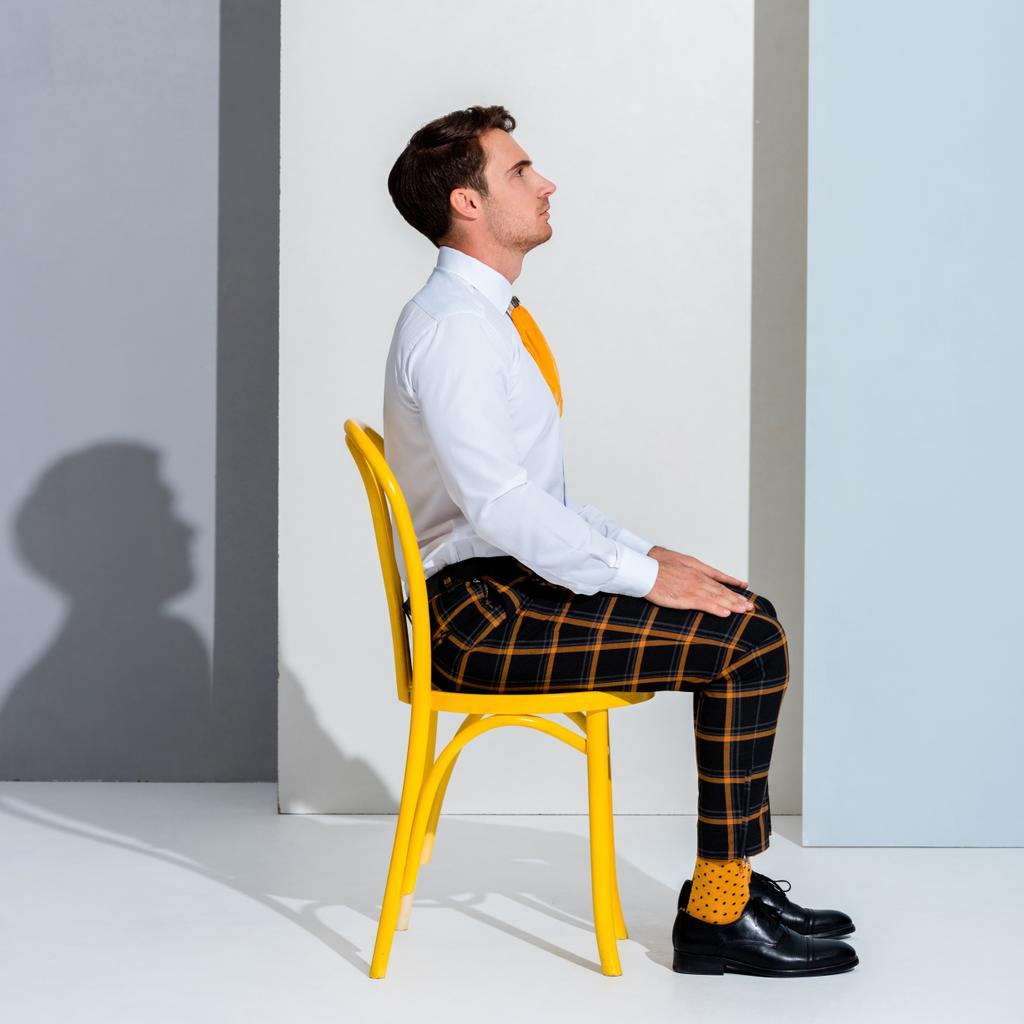 πλαϊνή άποψη του όμορφου άνδρα με καρό παντελόνι κάθεται σε λευκό και γκρι  - Φωτογραφία, εικόνα