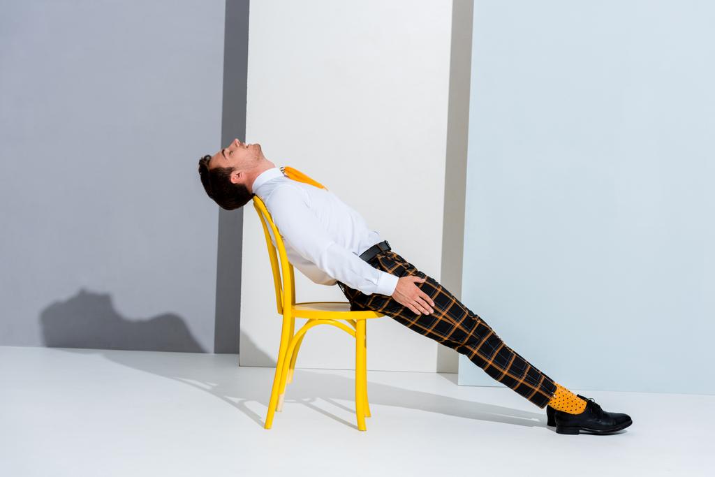 férfi kockás nadrágban feküdt sárga széken fehér és szürke - Fotó, kép