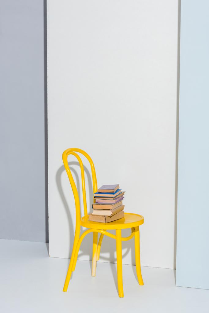 Gelber Stuhl mit Büchern auf weiß und grau  - Foto, Bild
