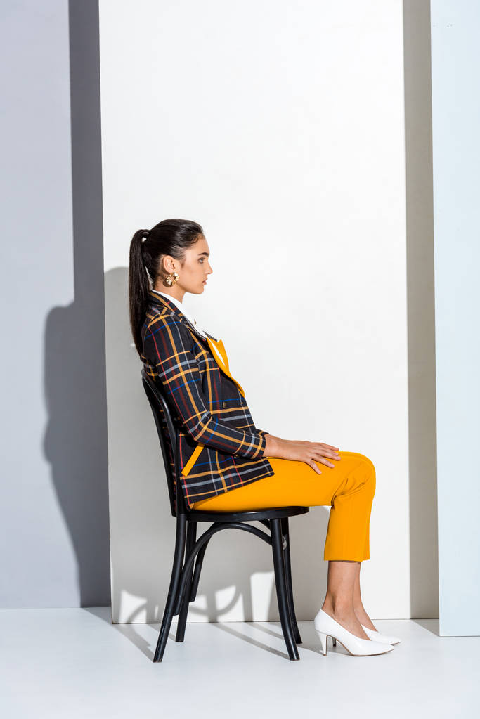 вид сбоку привлекательной молодой женщины, сидящей на стуле на сером и белом
  - Фото, изображение
