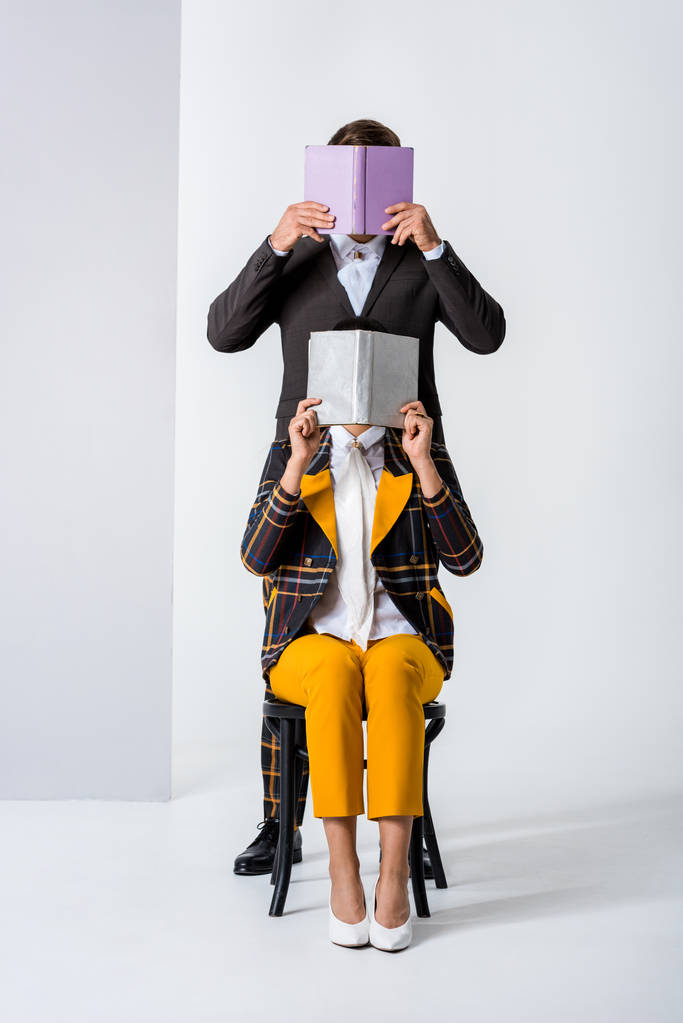 elegante hombre y mujer cubriendo caras mientras sostiene libros en blanco
  - Foto, Imagen