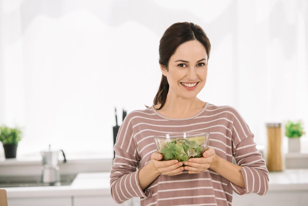 新鮮な野菜サラダで椀を持ちながらカメラで微笑む幸せな若い女性 - 写真・画像
