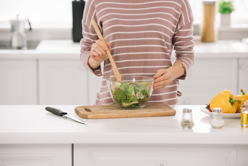 частковий вид на жінку, що змішує свіжий овочевий салат, стоячи за кухонним столом
 - Фото, зображення
