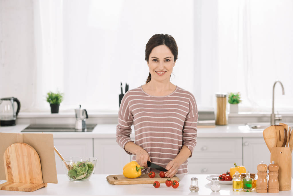 joven, mujer feliz cortando verduras frescas en la tabla de cortar y mirando a la cámara
 - Foto, Imagen