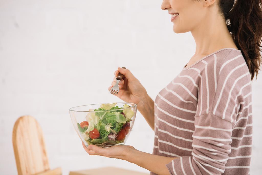 обрезанный вид улыбающейся женщины, держащей миску со свежим овощным салатом
 - Фото, изображение