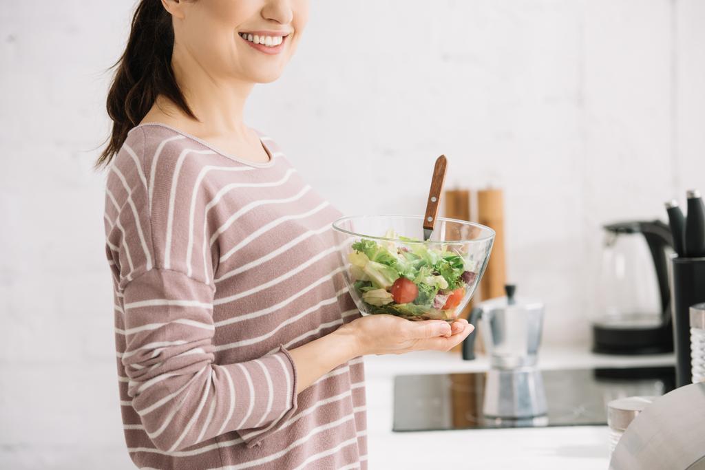 vue recadrée d'une jeune femme souriante tenant un bol avec salade de légumes
 - Photo, image