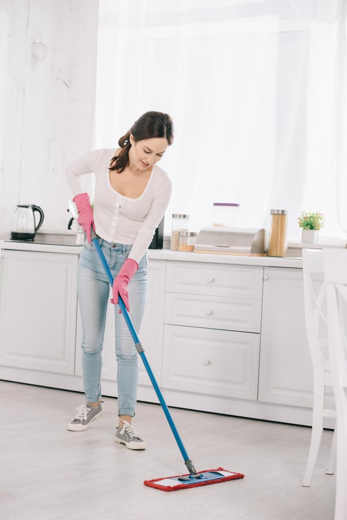 приваблива, молода домогосподарка миє підлогу на кухні з мопедом
 - Фото, зображення