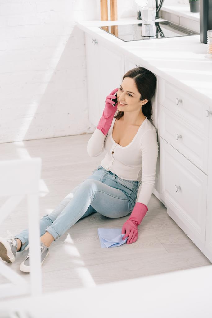 台所の床に座ってスマートフォンで話している陽気な主婦の選択的な焦点 - 写真・画像