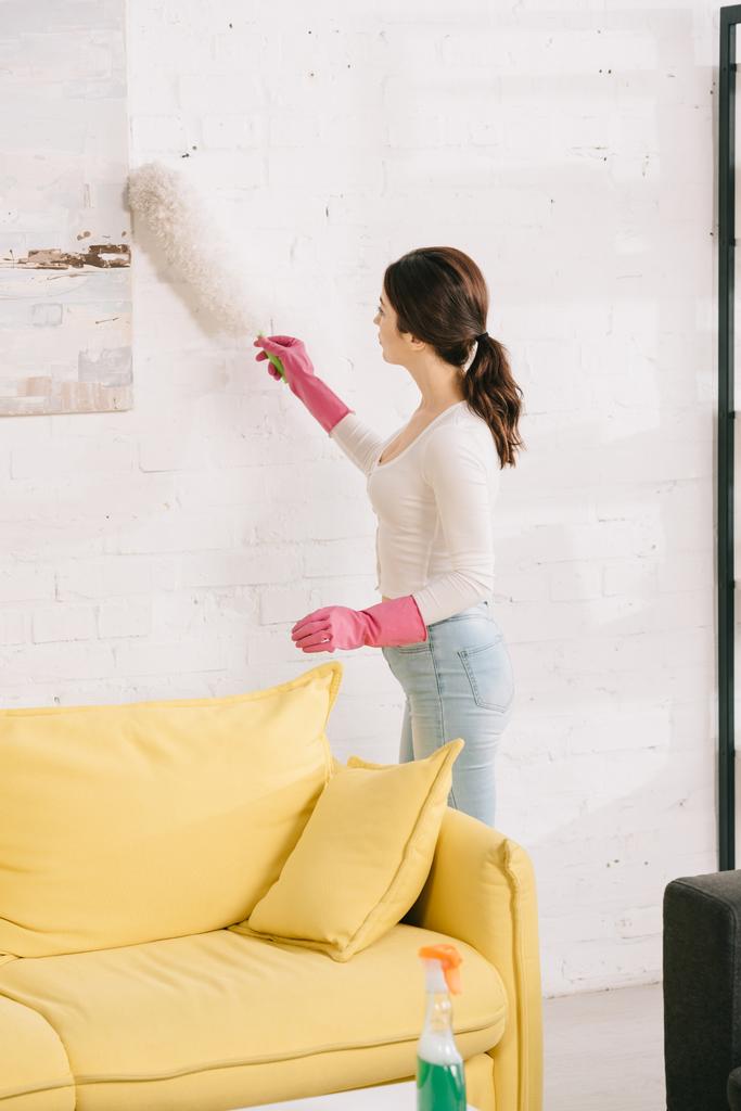 jovem dona de casa limpeza foto na parede com escova de poeira
 - Foto, Imagem