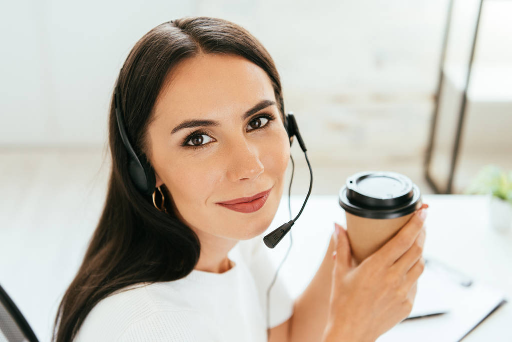 positive broker in headset holding disposable cup in office  - Photo, Image