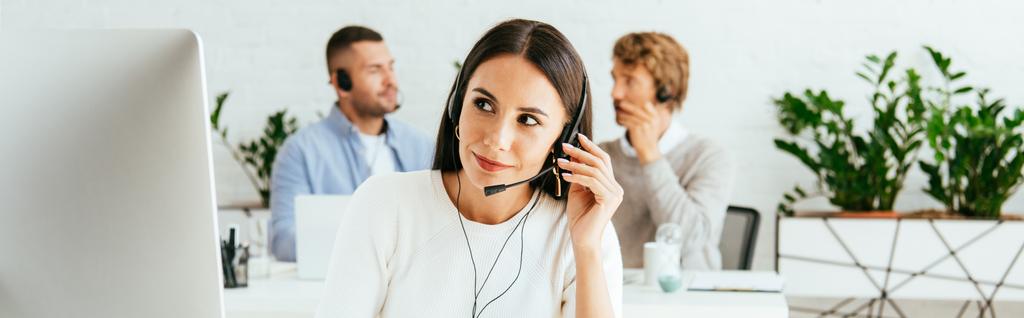 panoramic shot of attractive broker touching headset near coworkers in office  - Photo, Image