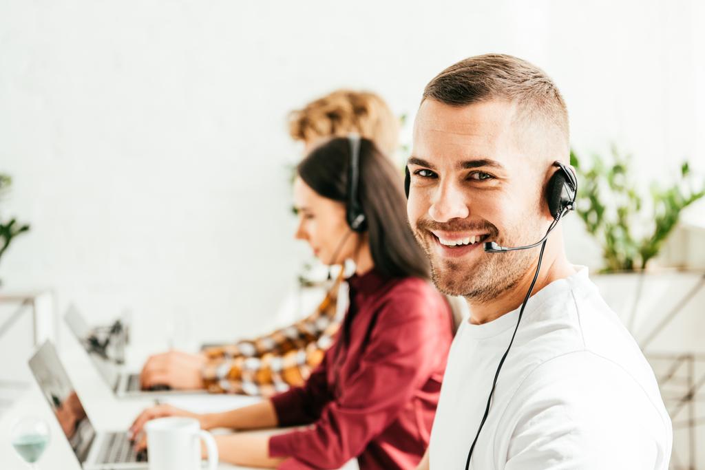 selective focus of cheerful broker in headset working in office with coworkers  - Photo, Image