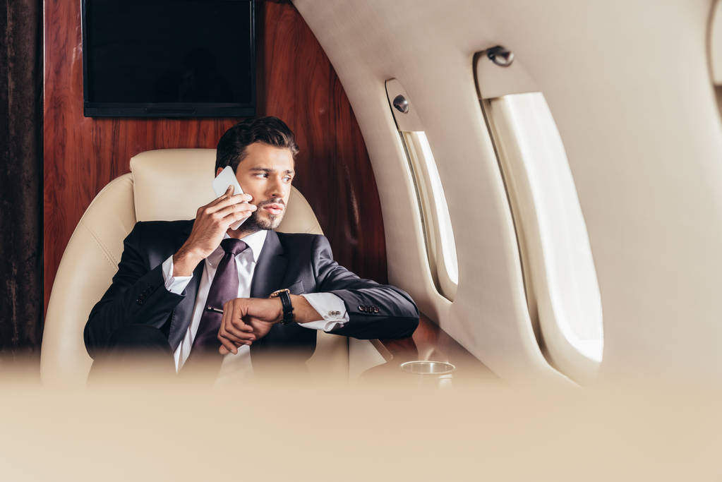 enfoque selectivo de hombre de negocios guapo en traje hablando en el teléfono inteligente en avión privado
  - Foto, imagen