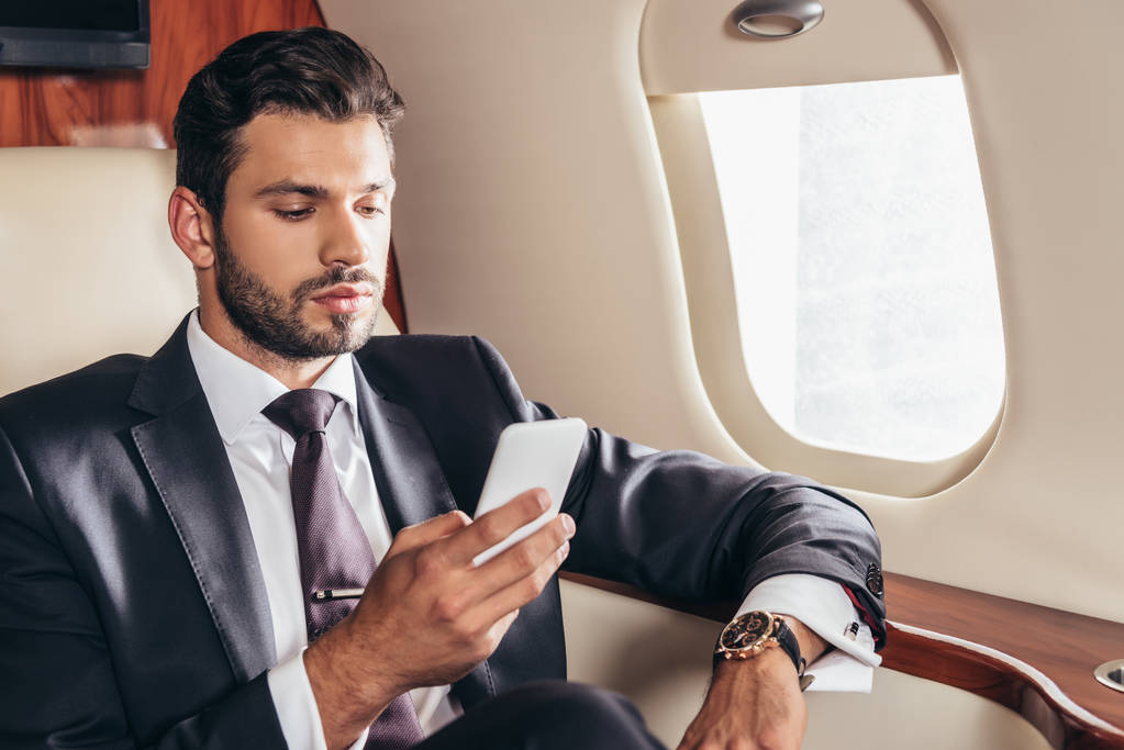bell'uomo d'affari in giacca e cravatta con smartphone in aereo privato
  - Foto, immagini