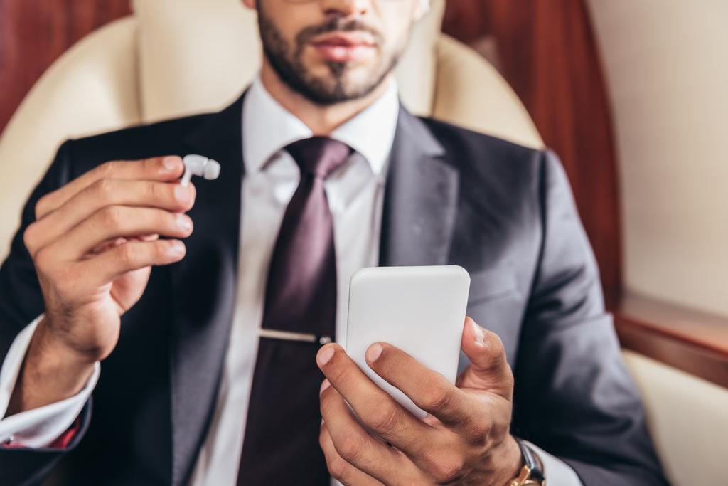 обрезанный вид бизнесмена, держащего наушники и использующего смартфон в частном самолете
  - Фото, изображение