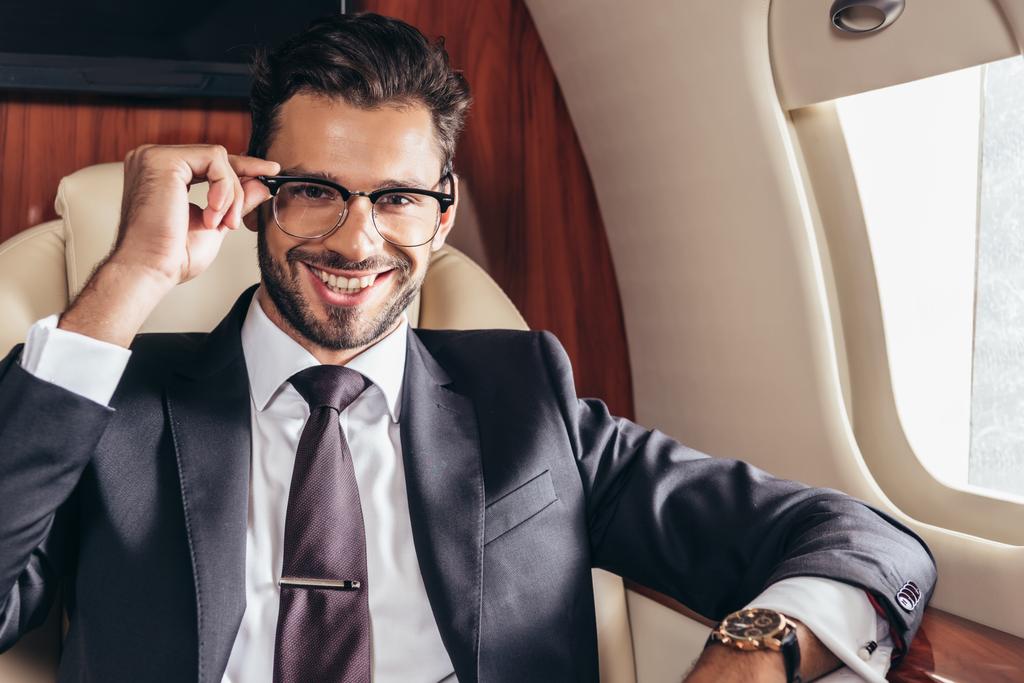 Gözlüklü yakışıklı iş adamı gülümseyerek özel uçakta kameraya bakıyor.  - Fotoğraf, Görsel
