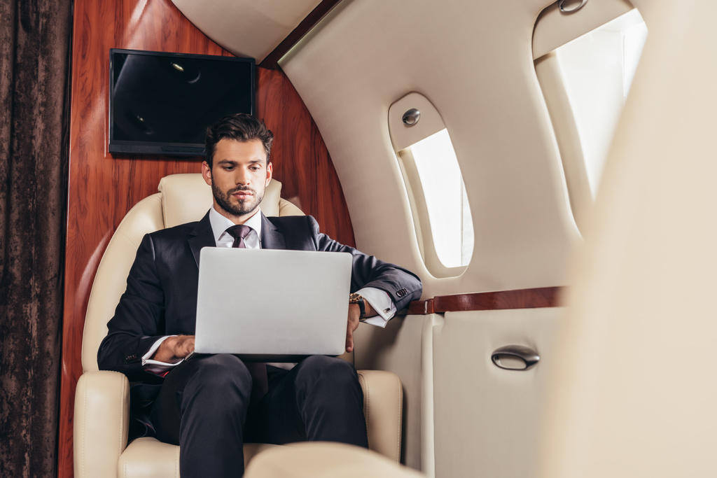 selectieve focus van knappe zakenman in pak met laptop in prive-vliegtuig  - Foto, afbeelding