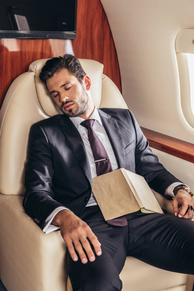 knappe zakenman in pak met boek slapen in prive-vliegtuig  - Foto, afbeelding