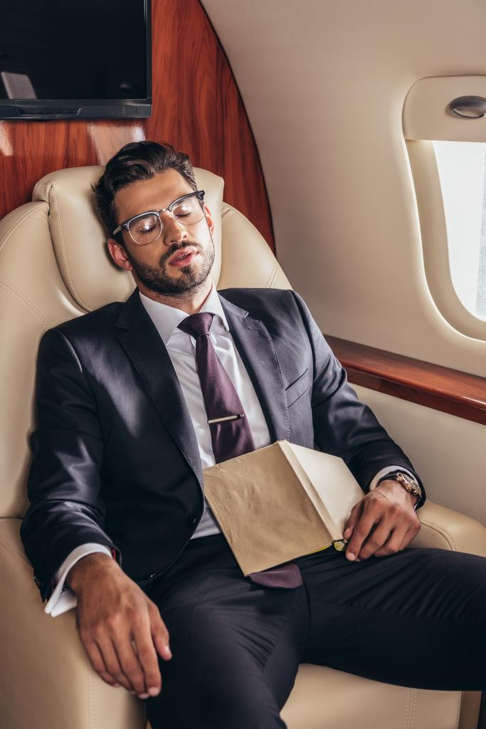 przystojny biznesmen w garniturze z książki śpi w prywatnym samolocie  - Zdjęcie, obraz