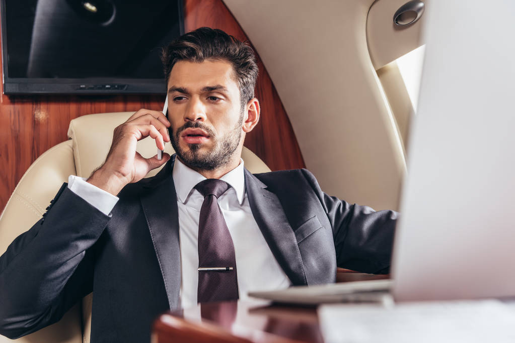 красивый бизнесмен в костюме разговаривает по смартфону в частном самолете
  - Фото, изображение