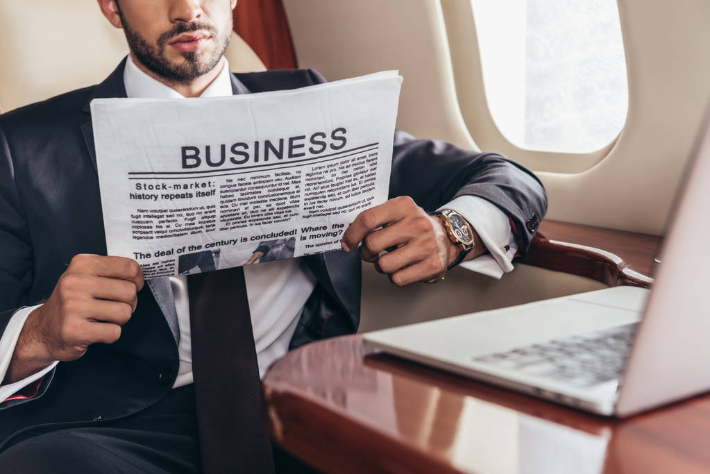 スーツ姿のビジネスマンが民間航空機でビジネス新聞を読む姿を切り取り  - 写真・画像