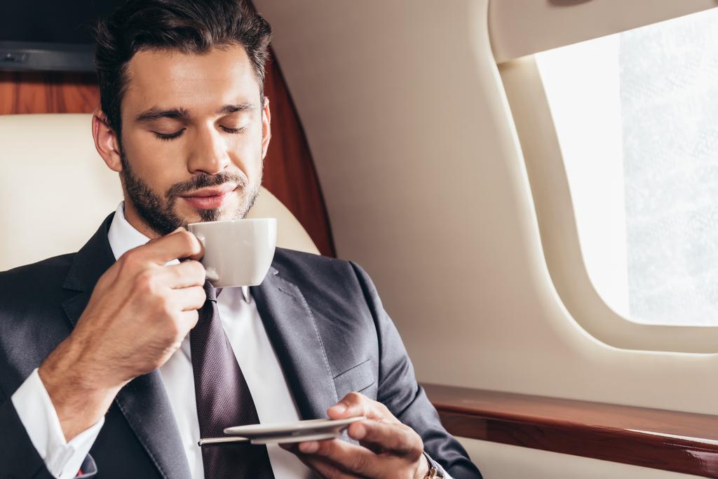 przystojny biznesmen w garniturze pachnący filiżanką kawy w prywatnym samolocie  - Zdjęcie, obraz