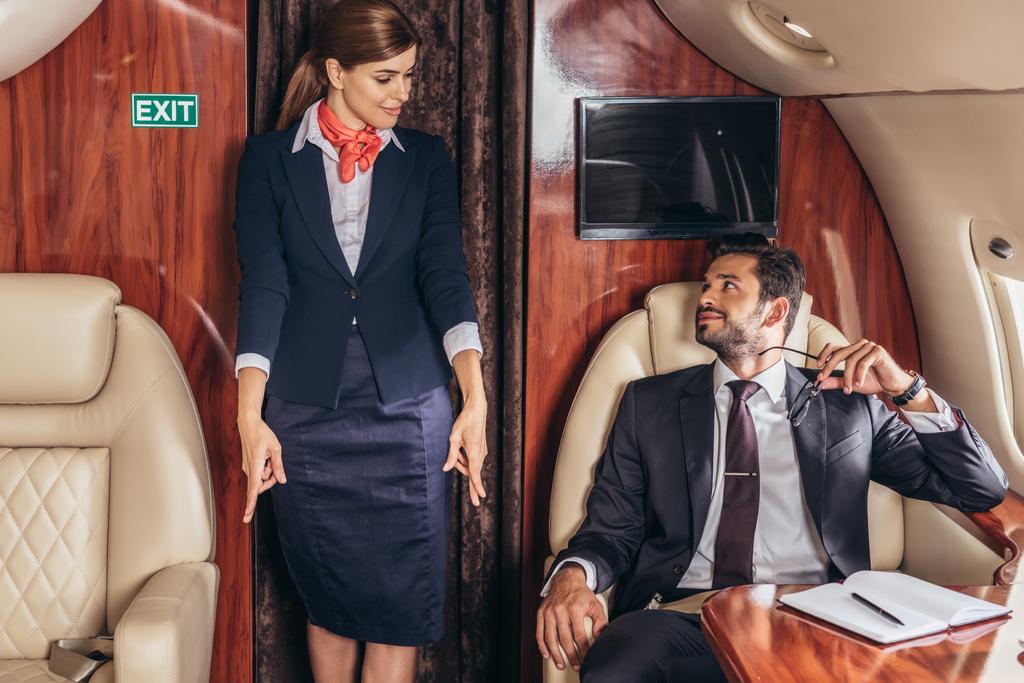 красивий бізнесмен у костюмі, дивлячись на стюардесу в приватному літаку
  - Фото, зображення