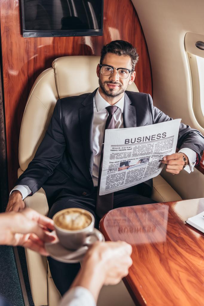 自家用機内でハンサムなビジネスマンにコーヒーカップを与える客室乗務員のクロップドビュー  - 写真・画像