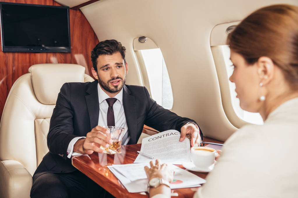 biznesmen ze szkłem pokazujący kontrakt bizneswoman w prywatnym samolocie  - Zdjęcie, obraz