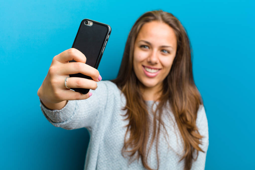 mujer joven con un teléfono móvil sobre fondo azul
 - Foto, Imagen