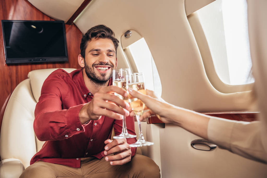 Lächelnder Freund und Freundin klirren mit Champagnergläsern im Privatflugzeug  - Foto, Bild