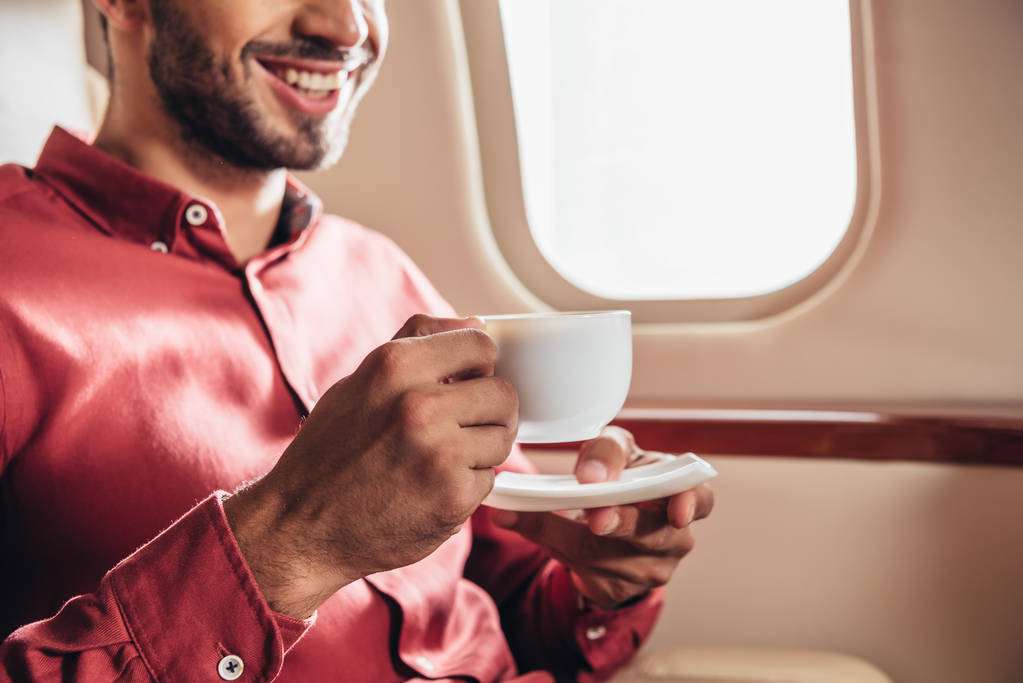 abgeschnittene Ansicht eines lächelnden Mannes im Hemd mit Pokal im Privatflugzeug  - Foto, Bild
